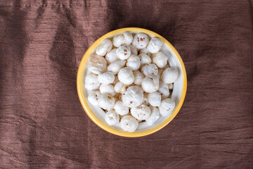 Top view of bowl having full of makhana in brown background.