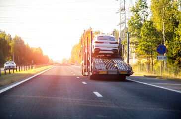 A truck with a semi-trailer for transporting cars on a country road in summer against the backdrop of a sunset. Concept international delivery of cars by car carrier. Copy space for text