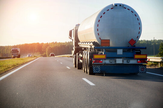 A truck tractor with a tank semi-trailer is transporting a hazardous flammable cargo - fuel. Truck with tank semi-trailer on highway against sunset in summer, copy space for text, international