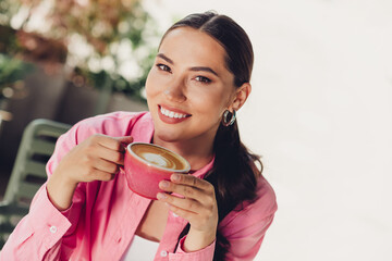 Elegant woman in a pink shirt enjoying a cappuccino outdoors on a sunny day, showcasing vibrant...
