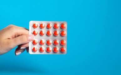 Blister with red pills in hand on blue background. Concept of chondroprotector pills for joint...