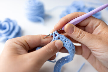 Close up of hands crocheting with blue yarn and hook