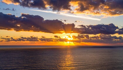 Obraz premium A vibrant sunset paints the sky above a tranquil ocean, showcasing dramatic clouds and warm hues.