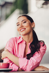 Charming young woman in a pink shirt enjoying urban outdoor setting, smiling with elegance and...