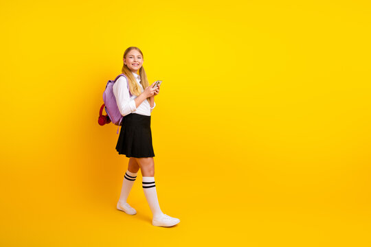 Cheerful schoolgirl in classic uniform holding a smartphone with a bright smile, backgrounded by vibrant yellow tones