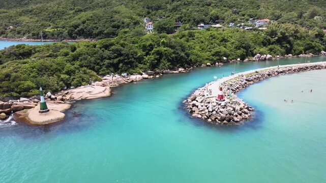Aerial view of the Barra da Lagoa Beach canal jetty with lighthouses for boats in Florian&oacute;polis, Santa Catarina, Brazil, with turquoise blue sea and mountains full of Atlantic forest