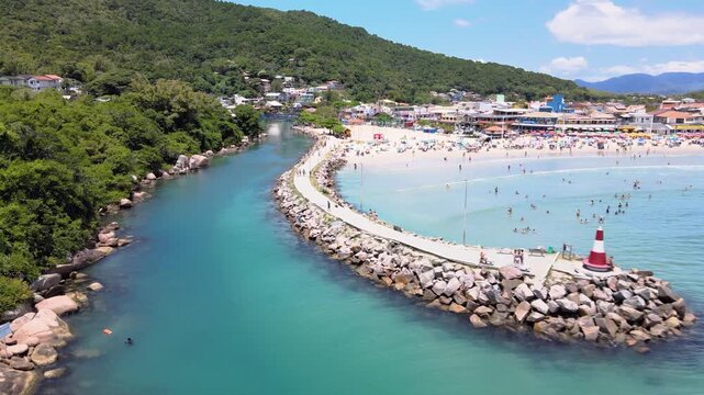 Aerial view of the Barra da Lagoa Beach canal jetty with a small lighthouse for boat entry and exit in Florian&oacute;polis, Santa Catarina, Brazil, with turquoise blue sea