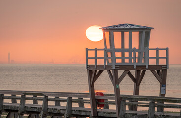 Luc-Sur-Mer, France - 08 10 2025: Panoramic view of the wooden pier in front of the sea named Fisherman's Pier at sunrise with the sun rising and Le Havre far away behind
