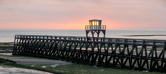 Luc-Sur-Mer, France - 08 10 2025: Panoramic view of the wooden pier in front of the sea named Fisherman's Pier at sunrise with the sun rising and Le Havre far away behind