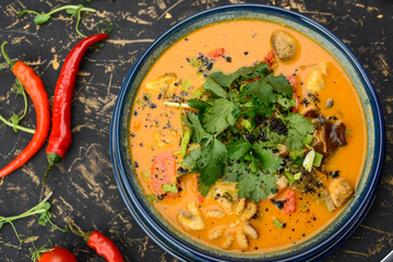 Tom yam soup with octopus pepper in a blue plate on a black background with decor