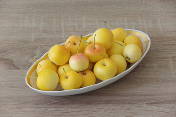 Small yellow apples. Chinese variety of small apples on a white plate against a wood texture background. Still life with apples. Close-up. Top view.