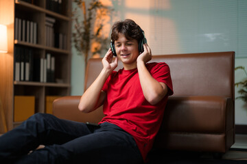 Obraz premium Young person relaxing, wearing wireless headphones, seated near sofa, immersed in music during downtime at home