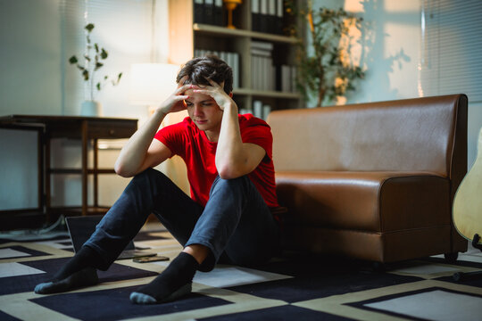 Depressed teen sitting alone on floor, head in hands, experiencing overwhelming emotional distress within domestic environment