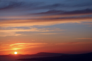 Colorful coastal sunset over calm sea with dramatic clouds.