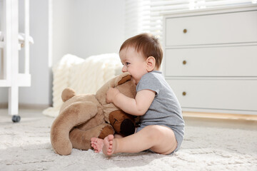 Cute little baby playing with teddy bear in room
