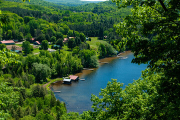 Obraz premium A breathtaking aerial shot captures a serene lake surrounded by lush greenery and scatterings of cozy houses, in a picturesque countryside during the summer season.