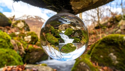 A crystal sphere captures a miniature waterfall cascading over mossy rocks, reflecting a mountainous landscape beyond.