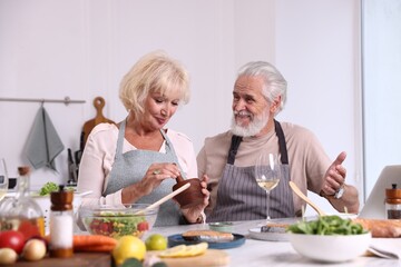 Elderly couple cooking together and drinking white wine at table indoors