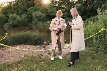 Forensic expertise. Detectives working at crime scene near lake outdoors, space for text