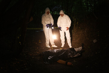 Forensic experts working at crime scene with dead man's body outdoors