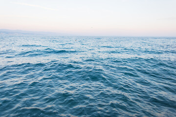 Calm blue sea with gentle waves under a clear sky at sunset. Minimal seascape background symbolizing peace, freedom. Blue ocean surface with calm waves fading into the horizon. Natural seascape