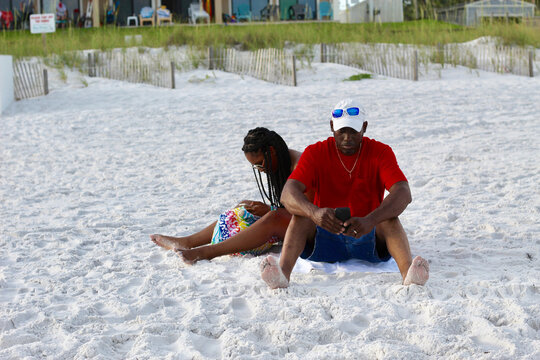A black father and daughter sitting on a beach 