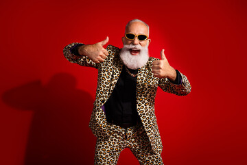 Fashionable older man in leopard print suit posing with a confident thumbs up gesture on bright red...