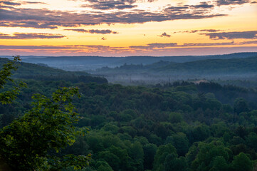 A colourful twilight over a rural foggy forest with rolling hills during the summer.