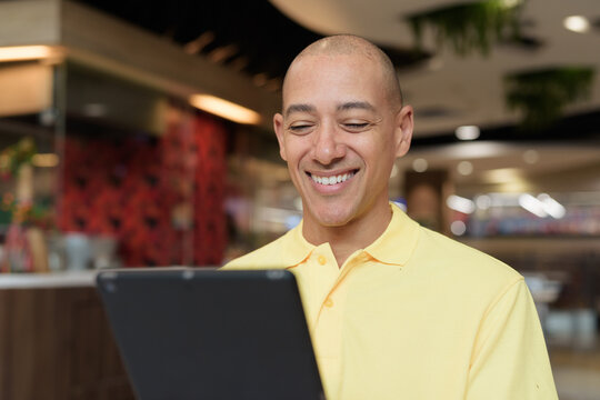 Middle-aged bald Hispanic man using tablet computer while dining at food court restaurant