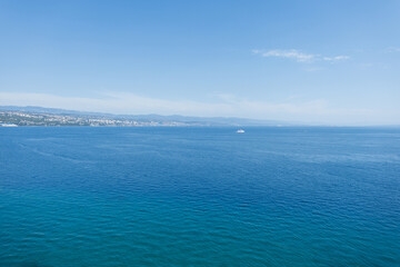 Coastal view of Opatija, Croatia, with calm Adriatic Sea and mountains with blue sky. Scenic seascape of Opatija, Croatia, city by the Adriatic Sea with distant hills and water.