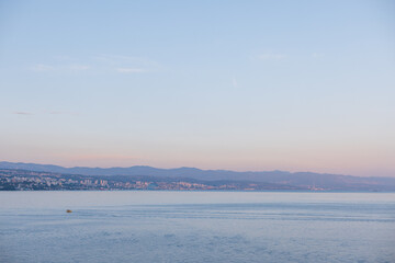 Coastal view of Opatija, Croatia, with calm Adriatic Sea and mountains in soft pastel evening light. Scenic seascape of Opatija, Croatia, city by the Adriatic Sea with distant hills and serene water.