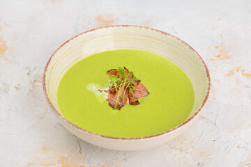 spinach cream soup with bacon and herbs in a white plate on a light background
