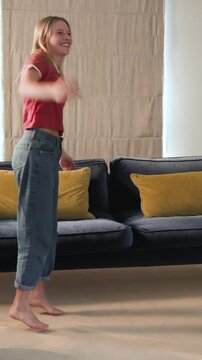 Vertical video: Woman dancer dancing to unseen beat, tossing hair and spinning on rug by sofa