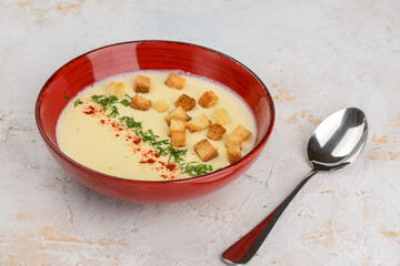 Cream of chicken soup with croutons in a red plate on a light background