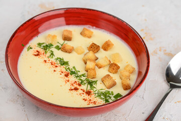 Cream of cream soup with croutons in a red plate on a light background macro