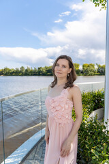 Beautiful woman in a pastel pink dress with floral details posing gracefully by a modern glass...