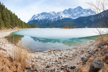 lake Eibsee with icy cover and reflecting mountain. Wetterstein alps with Zugspitze, bavaria