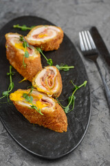 chicken rolls with filling in a black plate on a gray concrete background