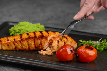 grilled salmon fillet in a black plate with tomatoes cut with a knife on a gray concrete background macro
