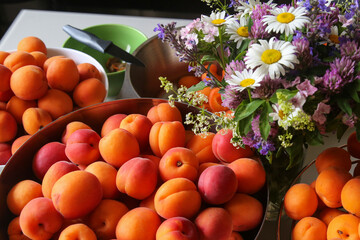 Ripe, juicy apricots in bowls and a bouquet of wildflowers made of daisies, clover, and other flowers