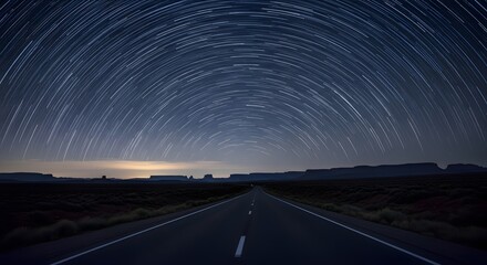 Photo of star trails arching over a long, empty road at night, capturing the vastness of the universe