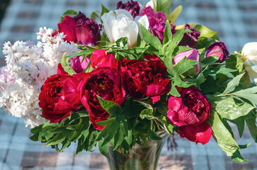 Vase with spring bouquet. Lilac, tulips and peonies in glass vase on tablecloth. Floral still life.