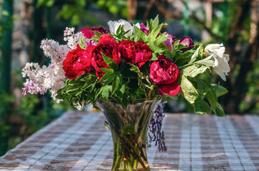 Vase with spring bouquet. Lilac, tulips and peonies in glass vase on tablecloth. Floral still life.