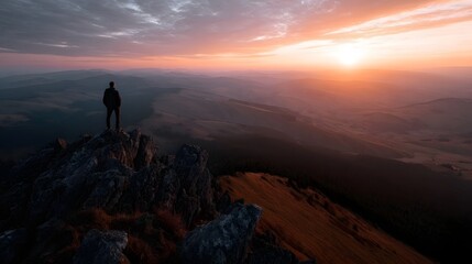 Obraz premium Lone hiker standing on a mountain peak overlooking a vast valley at sunrise