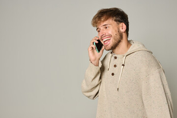 Laughing Caucasian man in beige hoodie talking on smartphone indoors