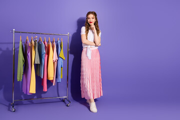Young woman standing by a clothing rack against a violet background showcasing colorful trendy...