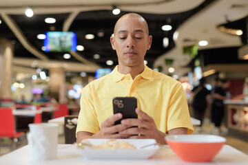 Mature bald Hispanic man using phone at indoors food court restaurant ready to eat chicken and rice