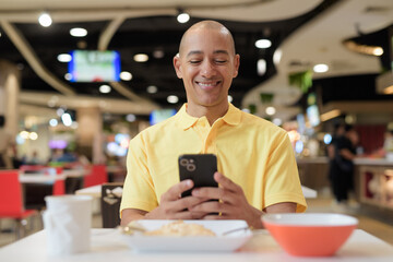 Mature bald Hispanic man using phone at indoors food court restaurant ready to eat chicken and rice