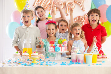 Birthday celebration. Kids at table with tasty cake and different treats in festive decorated room