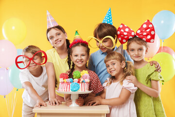 Birthday celebration. Happy kids with tasty cake and festive decor on orange background